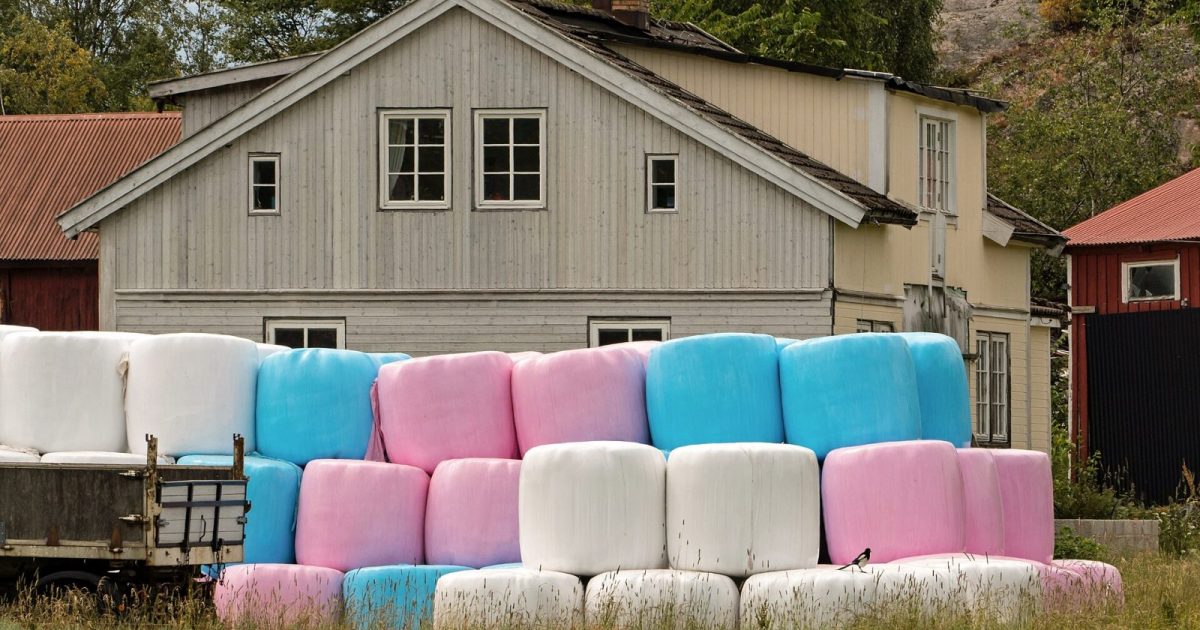 Inplastade balar staplade på en gårdsplan framför ett bostadshus
