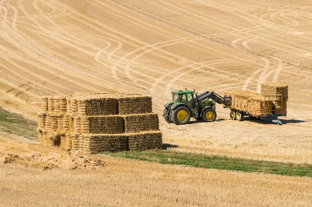 Traktor som lastar stora fyrkantsbalar i stapel