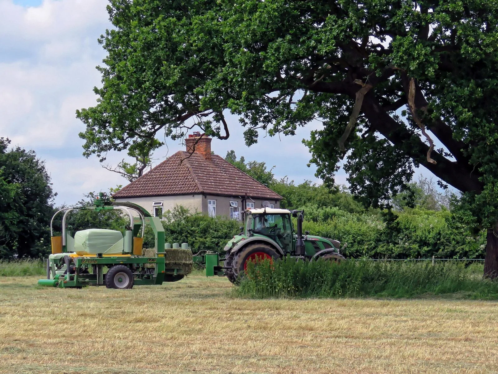 Traktor med balpress och inplastare vid gårdshuset