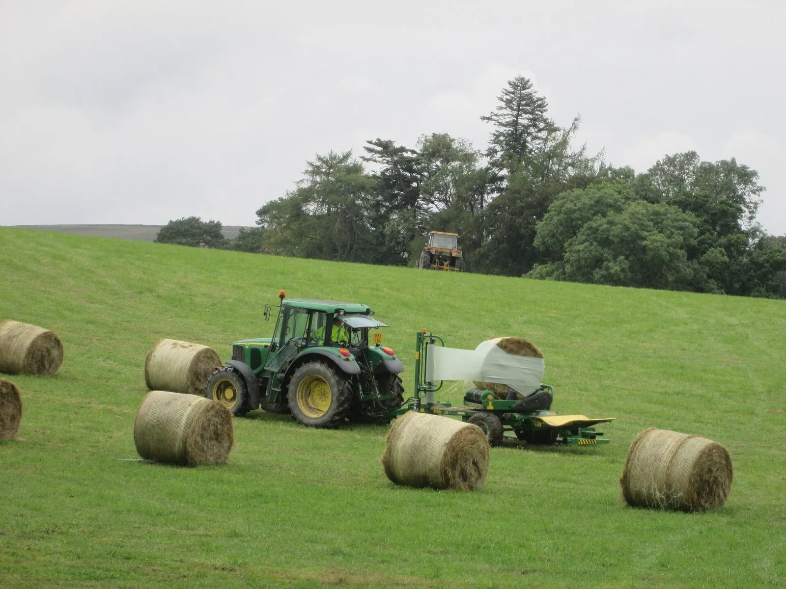 Traktor som plastar in rundbalar på vall